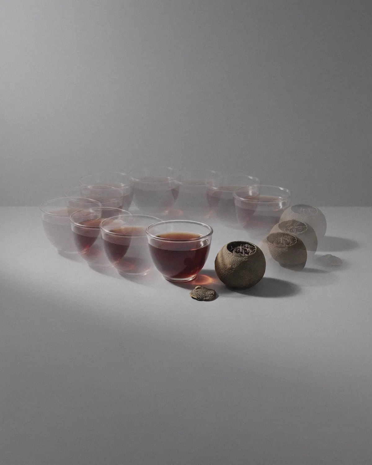 A ring of small glass cups of amber tea on a pale grey ground, a few tangerine pieces resting among them.