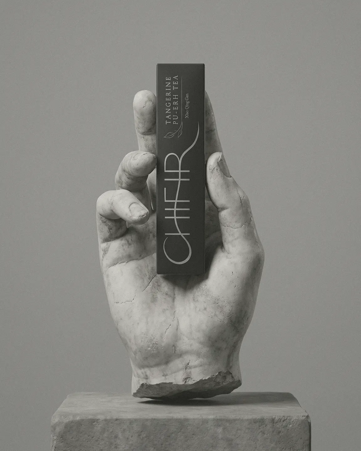 A white marble hand, carved in the classical manner, holding the black Tangerine Pu-erh carton upright on a stone plinth.