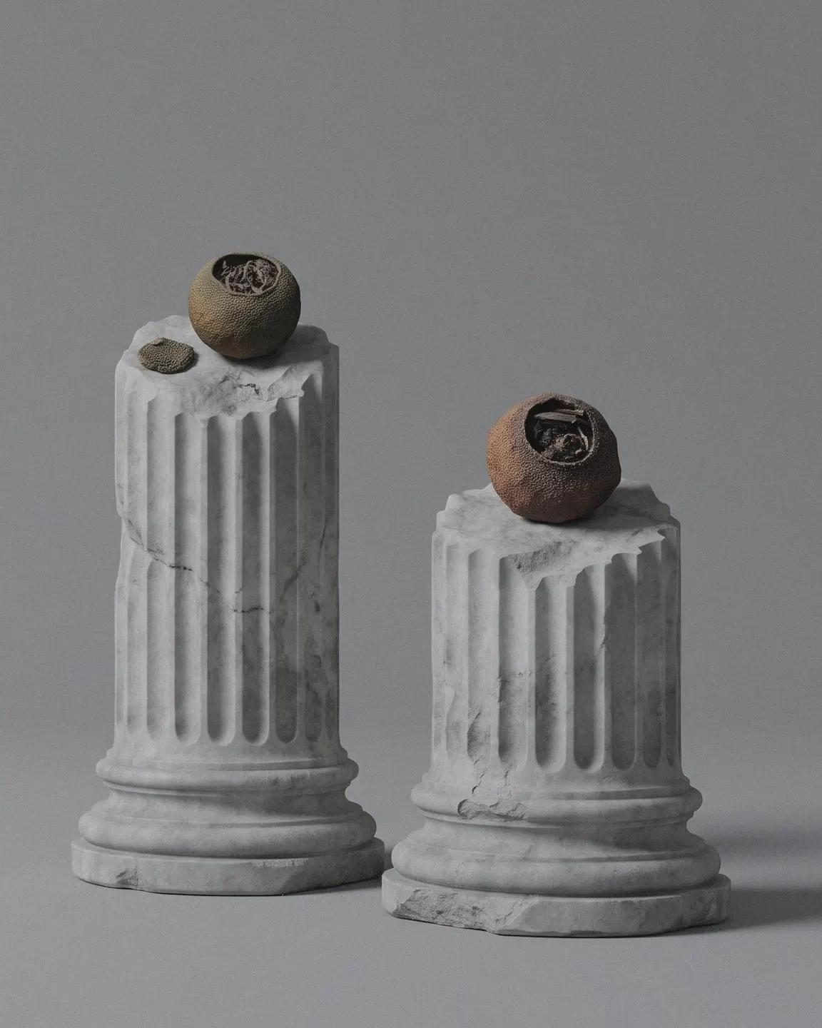 Two tangerine pieces, one on each of two broken marble columns of different heights, on a grey studio ground.