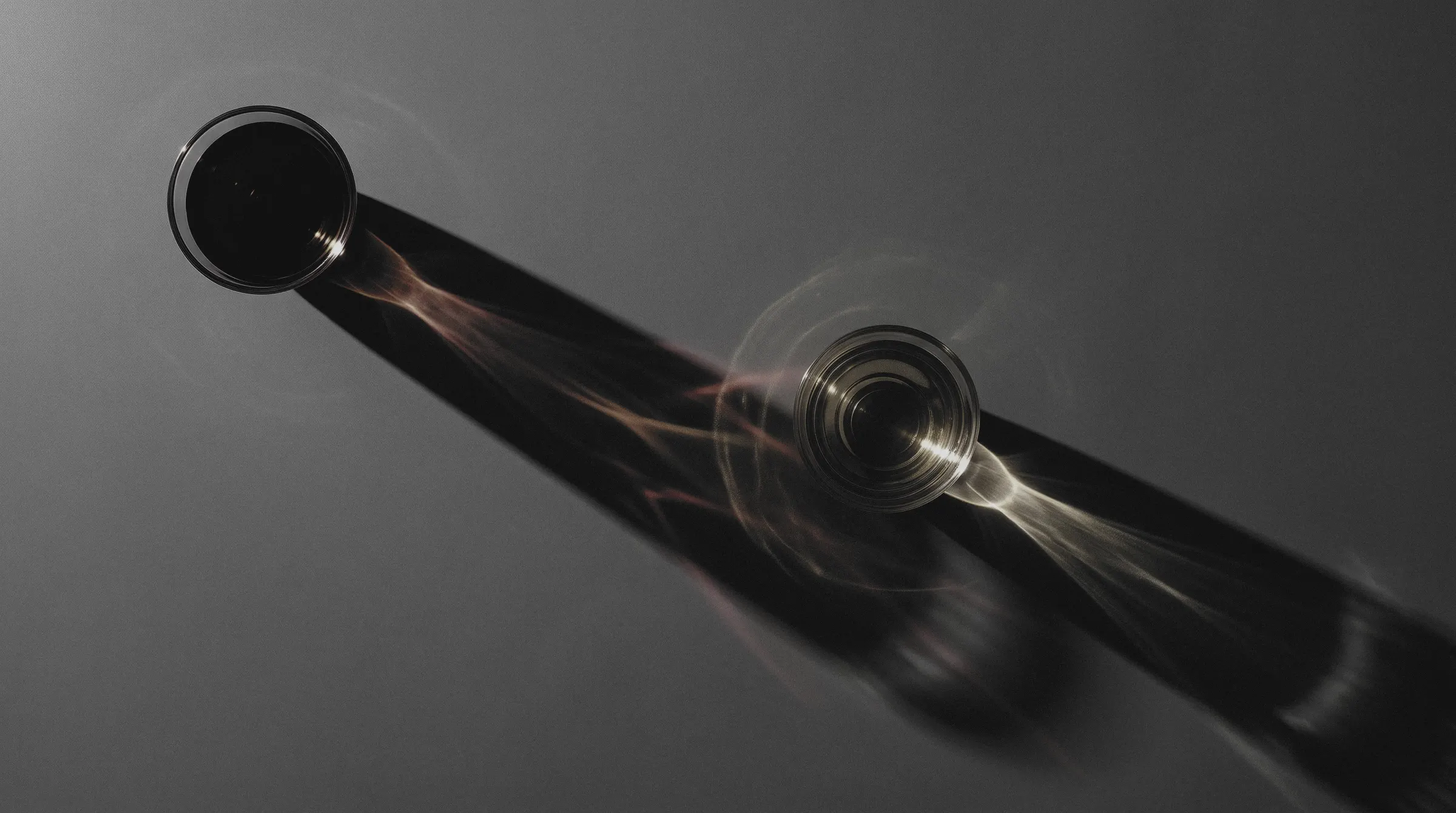Two small glass cups seen from above, one of dark pu-erh, one of pale white tea, throwing long streaks of red and gold light across a grey surface.