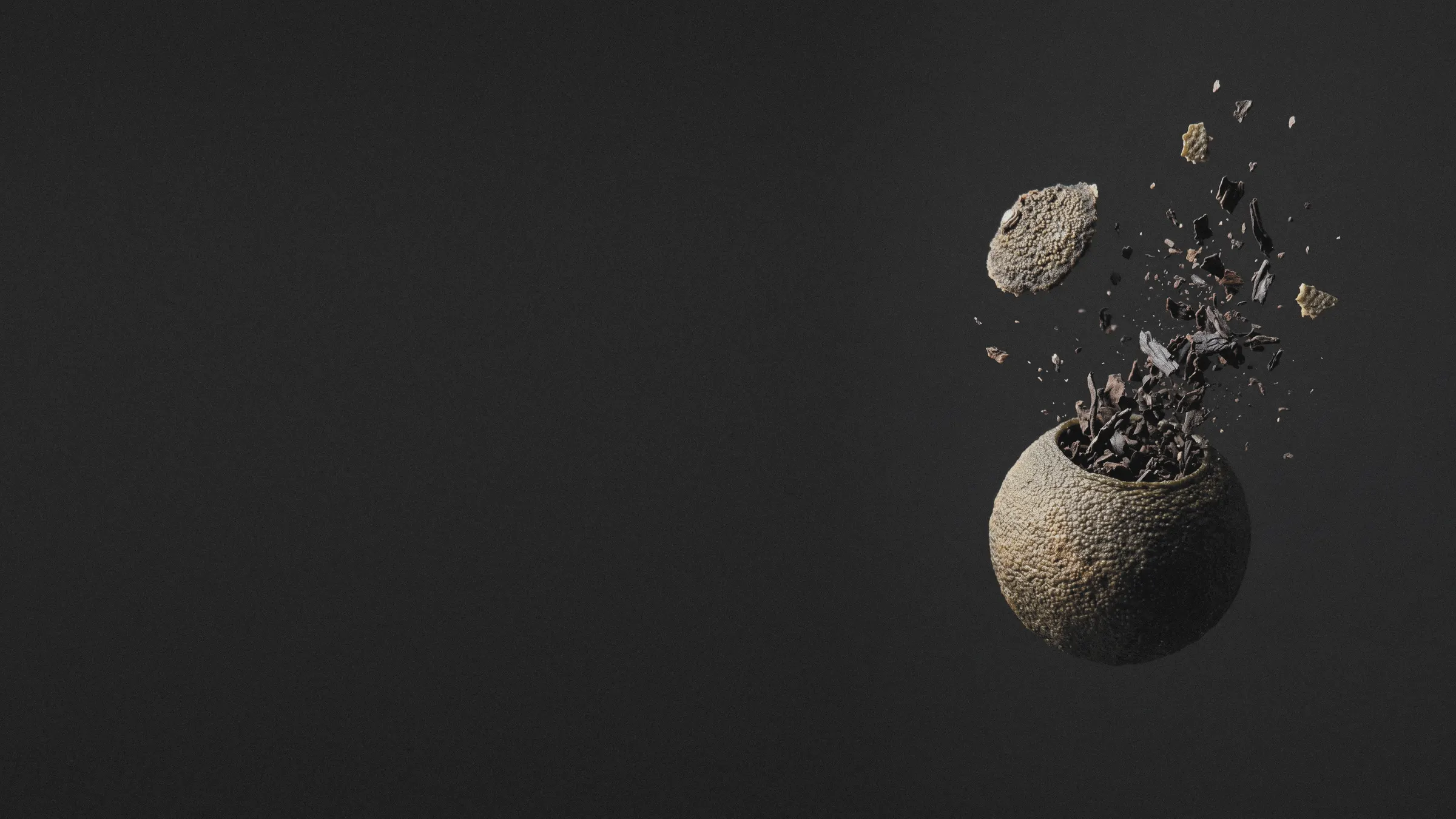 A dried tangerine piece bursting upward at the right, its lid and ripe pu-erh leaf flung into the air, on a charcoal studio ground that runs on to the left.